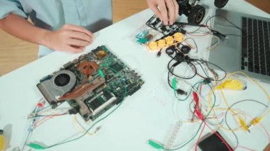Masadaki elektronik aletle ana kartı tamir eden çocuğa yakın çekim. Elektronik ekipmanlı bir lise öğrencisi elektrik panosunun en üst görüntüsü, kablo aletleri masanın etrafına saçılmış. Öğretim