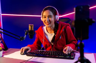 İnternet üzerinden kulaklık takıp gülümseyen Asyalı güzel kız flamasının sunucu kanalı izleyicilerle internet üzerinden konuşma yapıyor. Esport yetenekli takım oyuncuları neon mavi odada. Taktik.