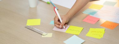 Genç yaratıcı iş kadınının yakın plan görüntüsü renkli yapışkan bir nota yazıp toplantı odasındaki beyin fırtınası zihin haritasına yerleştiriyor. Yaratıcı ve takım çalışması konsepti. Eline odaklan. Değiştirilmiş.