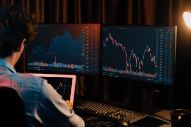 Dizüstü bilgisayara odaklanan genç yatırımcı, güncel pazar grafiğinin dinamik döviz kuru ekranını gerçek zamanlı olarak Neon Light Modern Ofis 'te yatırım yapan iki monitörle karşılaştırıyor. Toplayıcı.