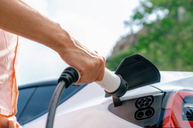Dışarıdaki şarj istasyonundan EV şarj aletini şarj etmek için elektrikli araca elle tak. Alternatif temiz ve sürdürülebilir enerji kavramına sahip taze gün ışığı ortamı. Kalıcı