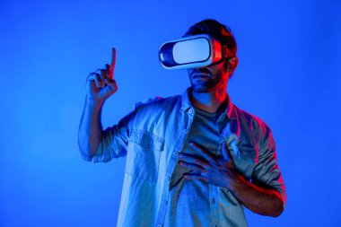 Gündelik giysileri olan beyaz bir adam VR gözlük takıyor ve havayı işaret ediyor. Zeki genç, yenilik kullanarak sanal gerçeklik dünyasını düşünürken renkli neon arka planda duruyor. Sapma.