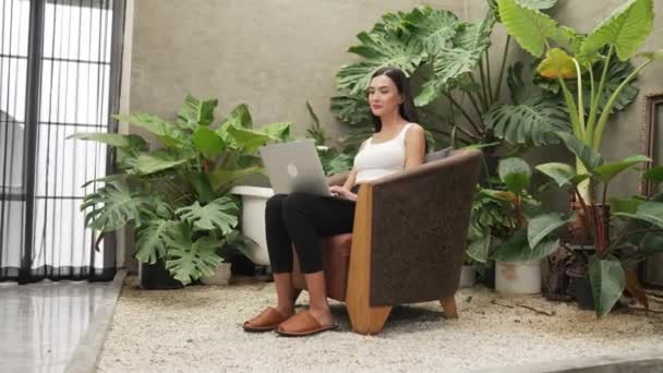 现代的年轻女子在电话中交谈 远程工作或在一个简约的建筑混凝土风格的夏天奇异的植物花园与热带植物的孤独中放松 — 图库视频影像