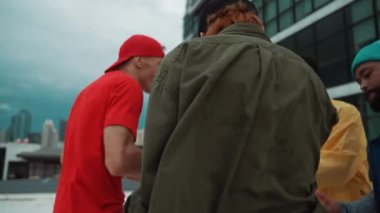Çok kültürlü veya çok kültürlü hipster grupları şık ve renkli giysiler giyerek çatıda şehir manzaralı ve gökyüzü kazıyıcılarıyla dans ederler. Canlı sokak dansı konsepti. Açık hava sporu 2024 hiphop..