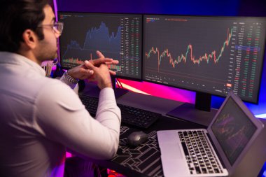 Akıllı tüccar işadamı, karanlık oda gecesinde neon ışıklı ofisteki arama pazarında yüksek kârla ekranda bilgisayar ve bilgisayar üzerinde dinamik borsa yatırımları üzerinde yoğunlaşıyor. Tahmin et..