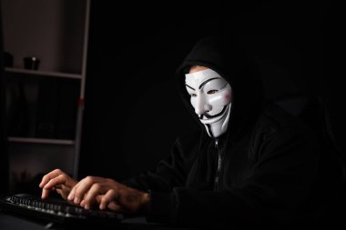 Beyaz gülümseyen isimsiz suçlu maskesi bilgisayar fidye sisteminde veri sunucusuna bilgisayar uygulaması tarafından virüs şifreleme programları yüklüyor. Bilgi bilgisayarda aranıyor. Tahmin et..