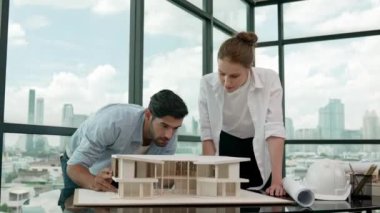 Profesyonel kooperatif iş arkadaşı ev modelini incelerken kalem kullanarak mimari modeli işaret eden yetenekli proje yöneticisi. Mimar mühendis takımı modeli belirlemek için birlikte çalışıyor. İzleme