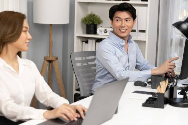 Gülümseyen Asyalı bir adam, yan görüntüdeki modern ofis çalışma masasında veri tabanını ararken günlük dizüstü bilgisayarla pazarlama raporu projesini planlarken kadın meslektaşıyla konuşuyor. İnfobahn.