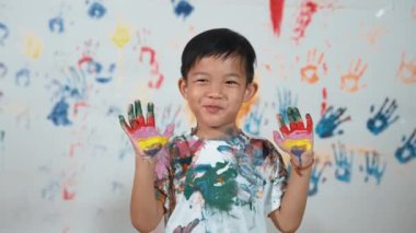 Asyalı mutlu öğrenci ellerini renkli lekeli elleri göster. Kameraya bakarken elleri lekeli, beyaz arka planda duran gülümseyen çocuk. Yaratıcı aktivite konsepti. Etkinlik.