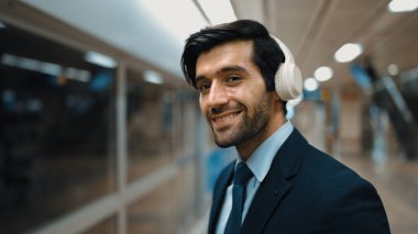 Tren istasyonunda dikilirken kulaklık takan ve müzik dinleyen zeki iş adamlarına yakın çekim. Profesyonel yönetici tren ya da metro beklerken kameraya bakıyor. Sevinçli..