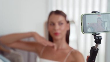 Genç sosyal medyum kadın moda videosu yapıyor. Blogcu kameraya selfie çubuğu ve ışık halkası kullanarak gülümserken, aynı zamanda ikna edici çevrimiçi kıyafetlerin izleyicilere veya takipçilere vlog satmasını sağlıyor. Düzenle