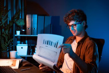 Genç işadamı, Neon Light Modern Ofis 'teki yeni proje surround çalışma masası için kağıt üzerinde tasarım düşünüyor. E-posta ile hediye göndermeden önce not defterine yeni bir iş düşünüyorum. Toplayıcı.