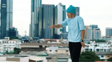 Beyaz tenli dansçı çocuk çatıda sokak dansı yapıyor şehir siteleriyle ya da şehirlerle. Genç adamın sokak dansı yaparken dondurucu poz vermesi. Açık hava sporu 2024. ÇalışmaComment.