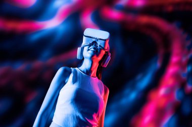Zeki bir kadın, metaevreni birbirine bağlayan VR kulaklık takan neon ışıklarla çevrili duruyor. Gelecekteki siber uzay topluluğu teknolojisi. Uzaklara bakan zarif bir kadın ve tatmin edici bir şekilde gülümsüyor. Halüsinasyon.
