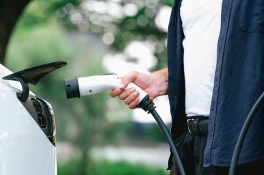 Yolculuk sırasında doğal orman ya da milli parktaki elektrikli araba için şarj olan bir adam. Tatil ve tatil boyunca çevre dostu seyahat. Yükselt