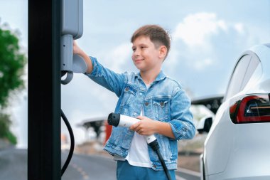 Küçük çocuk EV şarj istasyonundan çevre dostu elektrikli araba şarj ediyor. Temiz, yenilenebilir ve sürdürülebilir enerjiyle çalışan alternatif ulaşım için EV araba yolculuğu konsepti. Kalıcı