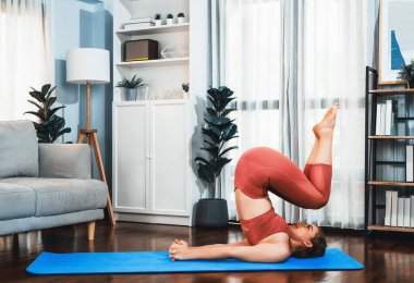 Spor kıyafetleri içinde esnek ve becerikli bir kadın evde egzersiz paspası üzerinde meditasyon pozisyonunda yoga yapıyor. Huzurlu ve huzurlu bir yoga yaşam tarzı..