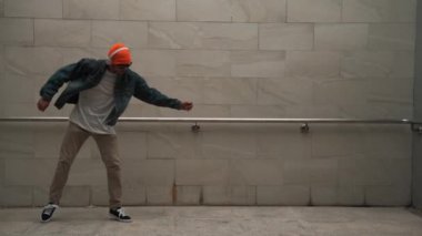 Asyalı akıllı hipster, kulaklık ve şık kıyafetler giyip hip hop şarkıları dinlerken gri arka planlı enerjik break dans gösterisi yapıyor. Açık hava sporu 2024. Hip hop hareketi. Yumuşak bir şekilde..