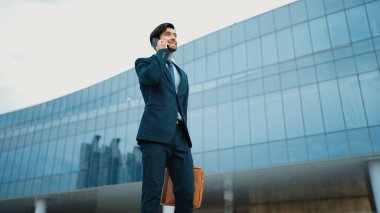 Akıllı iş adamı binada yürürken telefonla konuşuyor. İş planı, pazarlama stratejisi ya da çalışma hakkında konuşmak için akıllı telefonla konuşurken sokakta yürüyen mutlu bir yönetici. Sevinçli..