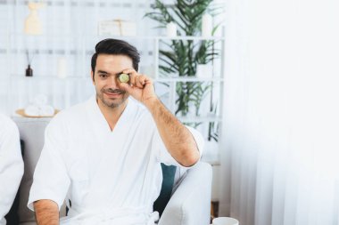 Elinde taze salatalık dilimleri tutan ve bornoz giyen bir adam tatil köyünde ya da otelde yüz bakımının keyfini çıkarıyor. Yüz ve güzellik tedavisi için cilt bakımı. Sessiz.