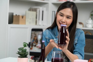 Gülümseyen, güzel Asyalı genç, lezzetli karışık çilek ve kiraz suyu detoksu içeceklerini inceleyen, sosyal medyada özel promosyon satışı için sağlıklı ürünler sergileyen. Taktik.