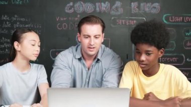 Kafkas öğretmeni mühendislik kodlarını öğretirken dizüstü bilgisayara bakıyor. Akıllı eğitmen mutlu lise öğrencileri öğrenirken ve programlama sistemini çalışırken dizüstü bilgisayar kullanarak çalışıyor.