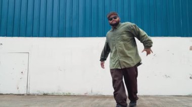Sokak ortasında mavi duvarlı hippi dansçı ayak basamağı. Asyalı break dansçı kollarını açarken sokak dansı yapıyor. Hip hop koreografı enerjik bir dans sergiliyor. Açık hava sporu 2024 hiphop..