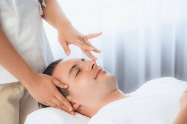 Beyaz adam stres önleyici kafa masajından ve lüks bir tatil beldesi veya otel spa salonundaki modern ışık ortamında yüz güzelliği eğlencelerini şımartmaktan hoşlanıyor. Sessiz.