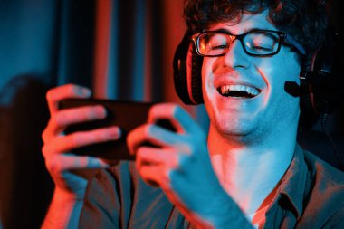 Gülümseyen genç oyun flaması takımı Esport ile online olarak akıllı telefon dövüşlerinde neon ışıklı odada kulaklık takarak oynuyorlar. Bir sonraki aşama için rakipleri kazanmak için strateji planı uyguluyorum. Toplayıcı.