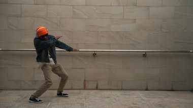 Asyalı akıllı hipster, kulaklık ve şık kıyafetler giyip hip hop şarkıları dinlerken gri arka planlı enerjik break dans gösterisi yapıyor. Açık hava sporu 2024. Hip hop hareketi. Yumuşak bir şekilde..