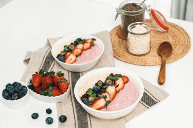 Meyvelerin sunduğu yoğurt malzemelerini çilek, yulaf, kuru üzüm ve nane şekeriyle süslenmiş Chia tohumu ile beyaza boyarız. Pembe arka plan. Sağlıklı süt ürünleri seti. Bireysel.