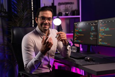 Bilgisayar ekranındaki yazılım geliştirme kodlamasına karşı poz vermek için akıllı bilişim geliştirici görünümlü kamera profilleri, neon ışıklı siber oda ofisinde program güncellemesi internet sitesi verileri sunuyor. Tahmin et..