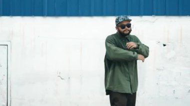 Sokak ortasında mavi duvarlı hippi dansçı ayak basamağı. Asyalı break dansçı kollarını açarken sokak dansı yapıyor. Hip hop koreografı enerjik bir dans sergiliyor. Açık hava sporu 2024 hiphop..