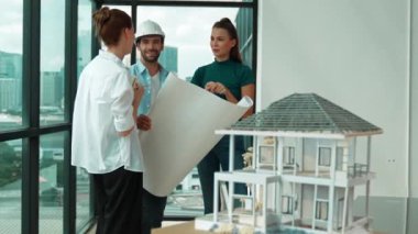 Profesyonel mimar mühendis ekibi konuşuyor, paylaşıyor, tasarım hakkında beyin fırtınası yapıyor. Yönetici planı dinlerken genç mimar plan yapıyor. İzleme