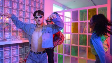 Asyalı adam gece kulübünde çeşitli neon ışıklarda dans ederken kolunu oynatıyor. Modern kulüpte çok kültürlü hippilerle dans eden şık elbiseli mutlu dansçı. Mutluluk.