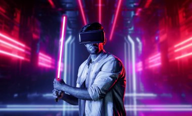 Lazer kılıcı tutan ve VR gözlük takan oyuncu. Beyaz adam, neon şatonun etrafında dikilirken görsel gerçeklik kulaklığı kullanıyor. Yenilik teknolojisi. Sapma.