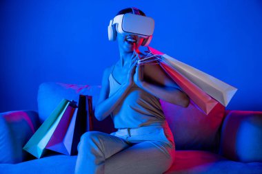 Akıllı kadınlar koltukta çantaların yanında otururlar. Meta-evrene bağlı VR kulaklık takarlar. Gelecekteki siber uzay topluluğu teknolojisi. Zarif bir kadın, meta dünyadaki çevrimiçi mağazalardan alışveriş yapmaktan hoşlanıyor. Halüsinasyon.