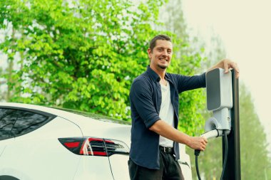 Yolculuk sırasında doğal orman ya da milli parktaki elektrikli araba için şarj olan bir adam. Tatil ve tatil boyunca çevre dostu seyahat. Yükselt