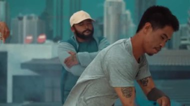 Bir grup çok kültürlü hippi çatıda işaret fişeği çalıyor. Zenci dumanı tutan çekici bir sokak dansçısı hip-hop müzik eşliğinde break dans yapıyor. Açık hava sporu 2024. Sokak dansı. hiphop.