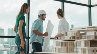 Gökdelene bakıp bir proje planı okurken, günlük kıyafetli akıllı mimar mühendis ekibi konuşuyor. Profesyonel yönetici takımı ev inşaatı hakkında beyin fırtınası yapıyor. Arkadan bak. İzleme