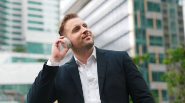 Erkek liderin etrafını sarın kulaklığı dinleyin ve neşeli ve motive edici bir şekilde rahatlatıcı müzikle dans edin. Becerikli proje yöneticisi şehir merkezinde akıllı telefon kullanırken rahat şarkılar dinlemeyi sever. Urbane.