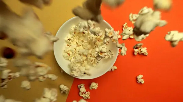 stock image Top down view of flying popcorn dropping at white bowl with yellow and orange background. Super slow motion shot of piles of fluffy salted popcorn falling in to the bowl. Macrography. Comestible.