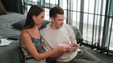 Genç çift, kredi kartıyla ödemek için internet üzerinden ödeme uygulaması ve dijital cüzdan kullanarak yatak odasında oturuyor. Mobil internet üzerinden alışveriş ve modern alımlar. Düzenle