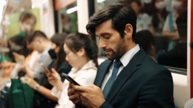 Gülümseyen beyaz iş adamı cep telefonuna bakıyor ya da trende otururken sosyal medya oynuyor. Çekici proje yöneticisi yoğun saatlerde toplu taşıma araçlarını kullanarak iş yerine gidiyor. Sevinçli..