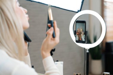 Sosyal medya için güzellik ve kozmetik video içeriği hazırlayan genç bir kadın. Güzellik blogcusu seyirciye güzellik hizmetini nasıl uygulayacağını ya da kamera karşısında takipçiyi nasıl izleyeceğini gösteriyor. Blithe