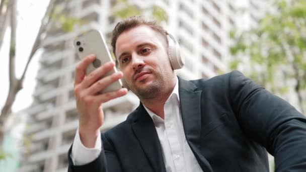 聪明的高加索商人戴着耳机 一边检查手机 一边看营销团队的销售报告 专业的经理工作在手机和数据分析方面 城市E — 图库视频影像