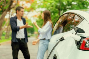 Sonbahar gezisi sırasında sonbahar ormanı EV arabasında elektrikli araba için şarj olan sevimli genç çift. Sonbahar tatilinde çevre dostu seyahat. Yükselt