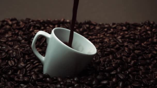 新鲜的浓缩咖啡倒在白杯里 里面堆满了咖啡豆 在杯子里倒入黑咖啡 配上褐色背景 种子撒在木制桌子上 靠近点慢动作可赔偿性 — 图库视频影像
