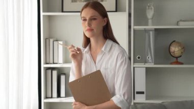 Klinikteki dost canlısı psikolog kadın. Profesyonel portresi. Kameraya bakıp psikolog muayenehanesine bakıyor. Tecrübeli ve kendinden emin psikolog.