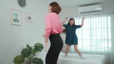 Yatak odasında Asyalı kızıyla müzik eşliğinde dans eden mutlu çekici anne. Beyaz anne dans eder ya da egzersiz yapar. Bu arada tatlı çocuk da müzik eşliğinde yatağa atlar. Aile eğlence konsepti. Pedagoji.